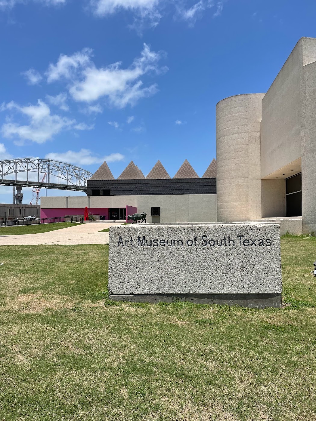 Exterior view of the Art Museum of South Texas with a sign in front and a clear blue sky.