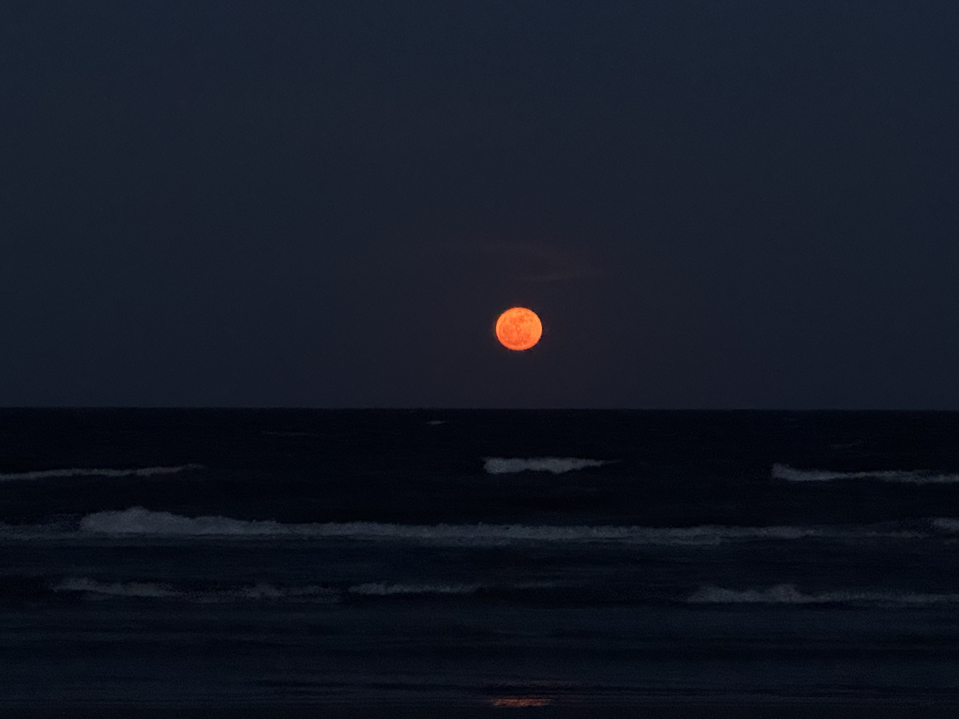 A large orange moon rises above the dark ocean, illuminated against a night sky.